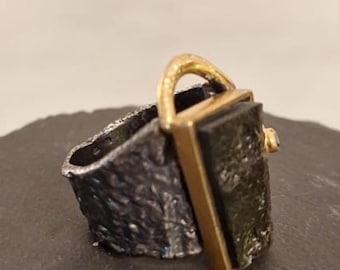 Anel feminino artesanal em prata 925 texturizada com granada moldavita e detalhes banhados a ouro – estilo brutalista.