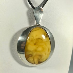 May include: A silver pendant with a large, oval-shaped amber stone. The pendant is suspended from a black leather cord.