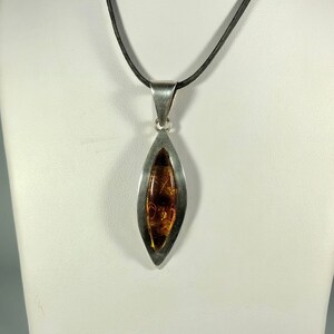May include: A silver pendant necklace with a teardrop-shaped amber stone set in a silver frame. The necklace is on a black cord.