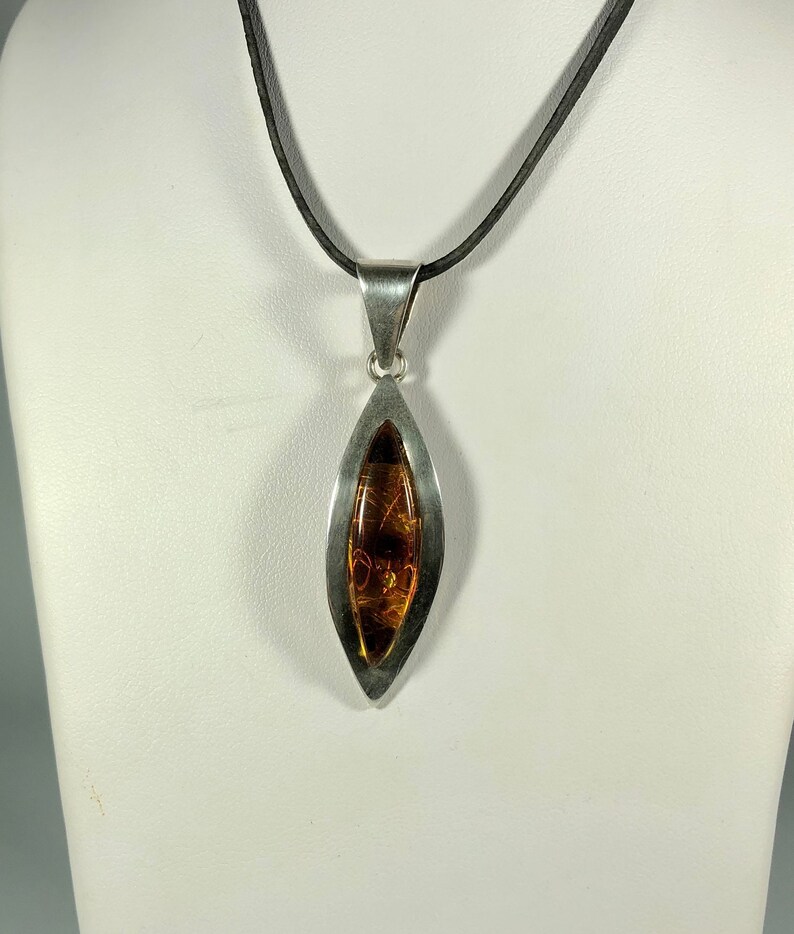 May include: A silver pendant necklace with a teardrop-shaped amber stone set in a silver frame. The necklace is on a black cord.