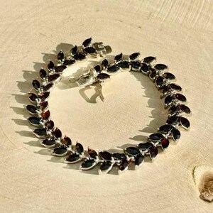 May include: A silver bracelet with a leaf design and dark red gemstones.