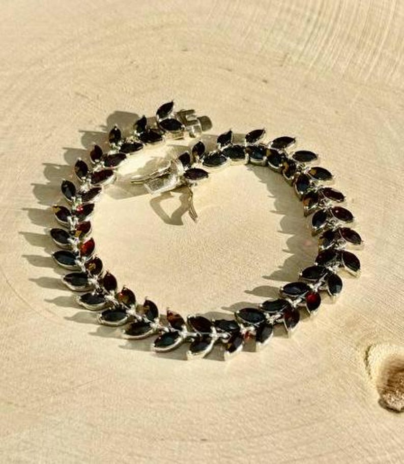 May include: A silver bracelet with a leaf design and dark red gemstones.