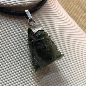 May include: A silver chain necklace with a green stone pendant carved with a face. The pendant is detailed with silver accents.