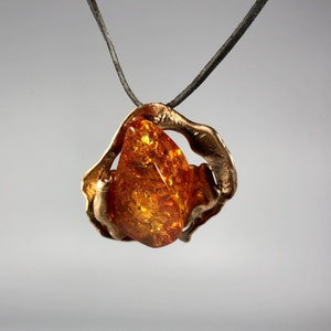 May include: A bronze pendant with a large amber stone. The pendant is shaped like a swirl and the amber stone is a teardrop shape.