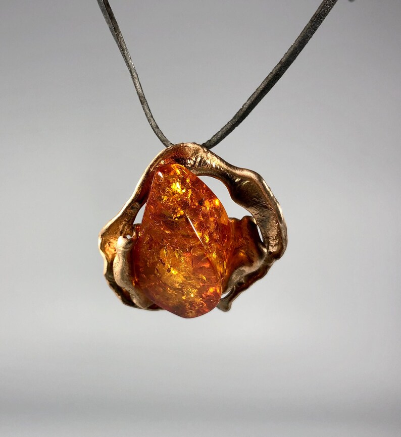 May include: A bronze pendant with a large amber stone. The pendant is shaped like a swirl and the amber stone is a teardrop shape.