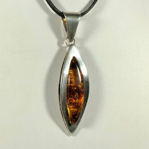 May include: A silver pendant with a teardrop-shaped amber stone. The pendant is on a black leather cord.