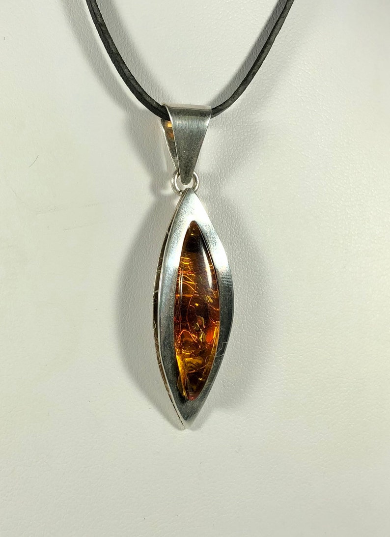 May include: A silver pendant with a teardrop-shaped amber stone. The pendant is on a black leather cord.
