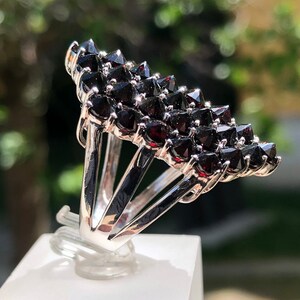 Pode incluir: Um anel de prata com um aglomerado de pedras de granada vermelho-escuro engastadas em forma triangular.