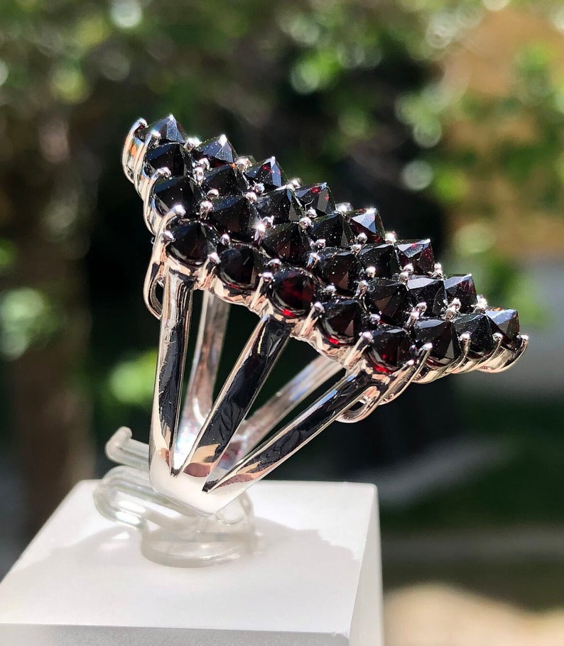 Pode incluir: Um anel de prata com um aglomerado de pedras de granada vermelho-escuro engastadas em forma triangular.