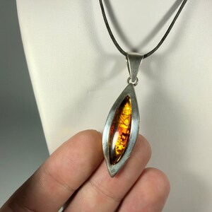May include: A silver pendant necklace with a teardrop-shaped amber stone set in a silver frame. The necklace has a black cord.