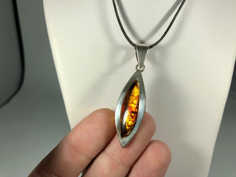 May include: A silver pendant necklace with a teardrop-shaped amber stone set in a silver frame. The necklace has a black cord.