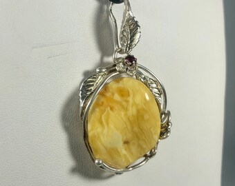 May include: A silver pendant with a large, oval-shaped amber stone set in a delicate silver leaf design. A small red gemstone is set at the top of the pendant.
