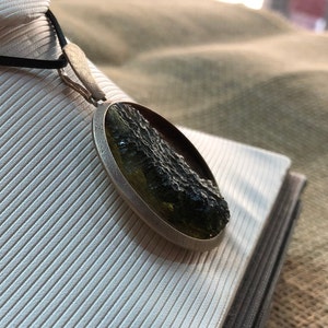 May include: A silver pendant with a round green and black stone. The stone has a rough, textured surface.