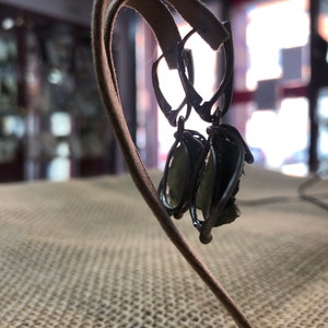 May include: A pair of silver earrings with green gemstone accents. The earrings are hanging on a brown leather display stand.