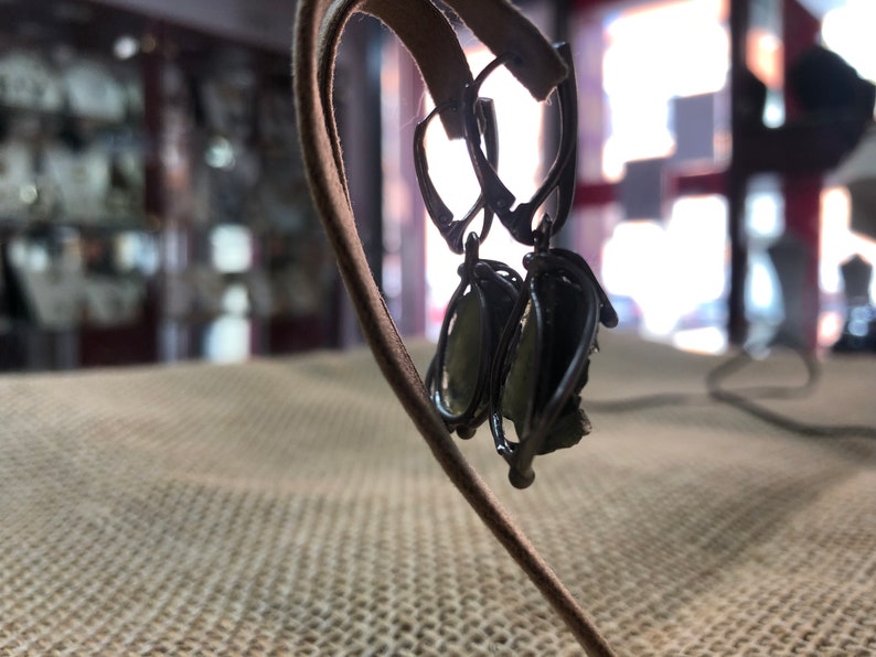 May include: A pair of silver earrings with green gemstone accents. The earrings are hanging on a brown leather display stand.