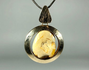 May include: A gold pendant necklace with a round frame and a large, amber-colored stone. The pendant is suspended from a black cord.