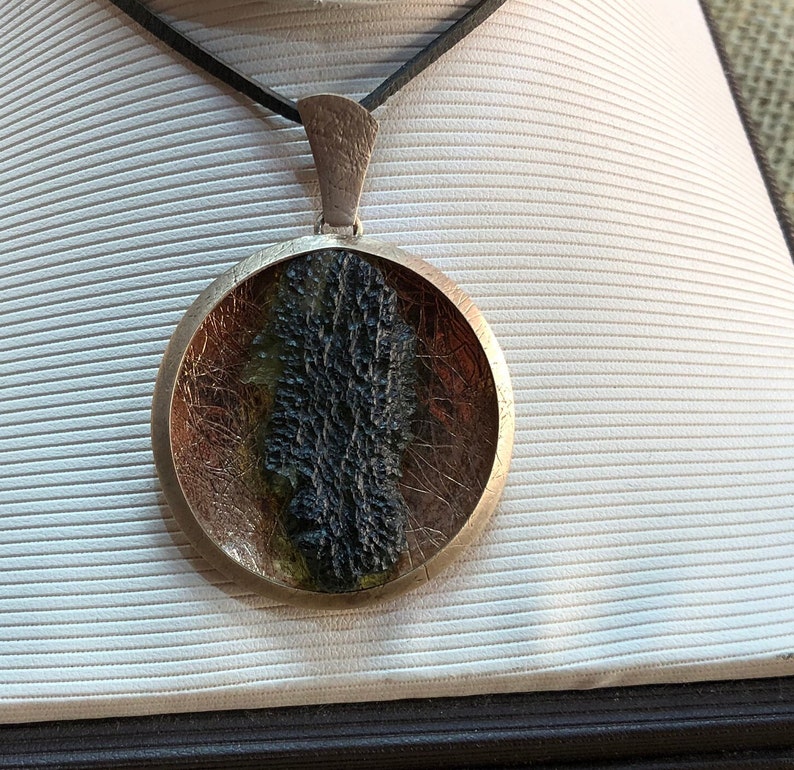 May include: A round silver pendant necklace with a black and green stone encased in resin. The stone has a rough, textured surface.