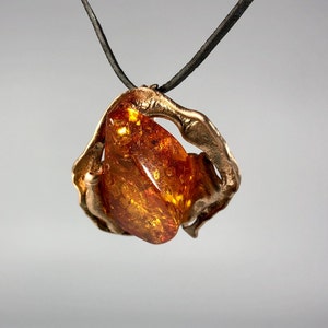 May include: A gold pendant necklace with a large amber stone set in a twisted metal frame. The necklace is on a black leather cord.
