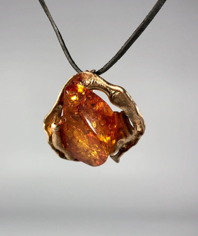 May include: A gold pendant necklace with a large amber stone set in a twisted metal frame. The necklace is on a black leather cord.