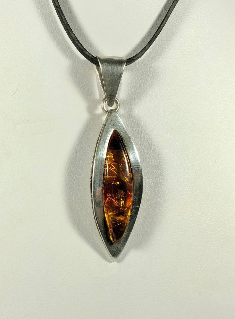 May include: A silver pendant necklace with a teardrop-shaped amber stone set in a silver frame. The necklace is on a black cord.