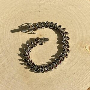 May include: A silver bracelet with a leaf design and red gemstones. The bracelet is open and ready to be worn.