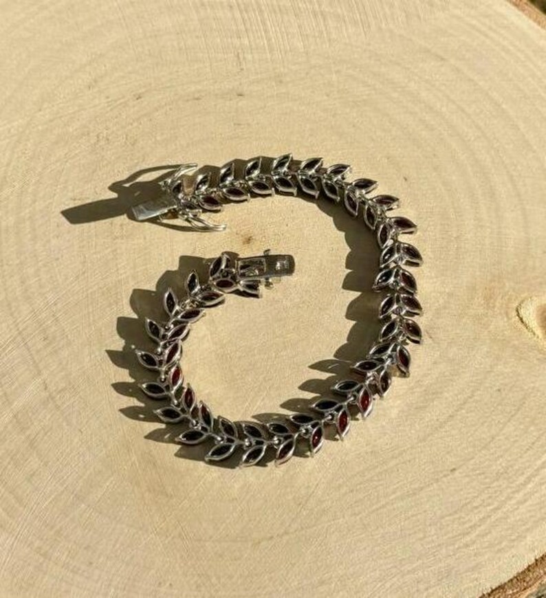 May include: A silver bracelet with a leaf design and red gemstones. The bracelet is open and ready to be worn.