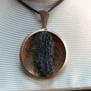 May include: A round silver pendant with a black and green resin inlay. The pendant is on a black leather cord.