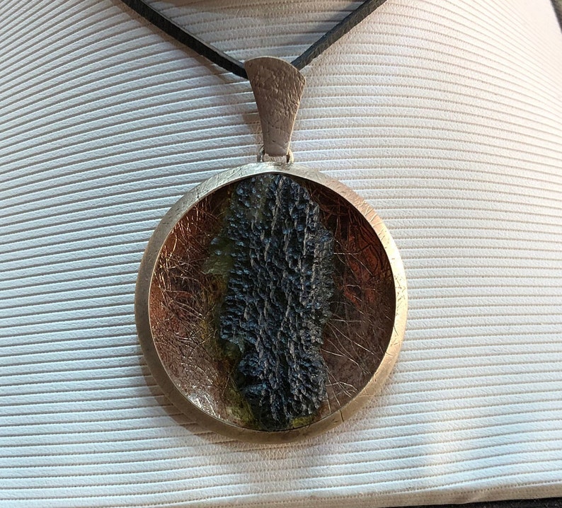 May include: A round silver pendant with a black and green resin inlay. The pendant is on a black leather cord.