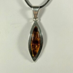 May include: A silver pendant necklace with a teardrop-shaped amber stone set in a silver frame. The necklace is on a black cord.