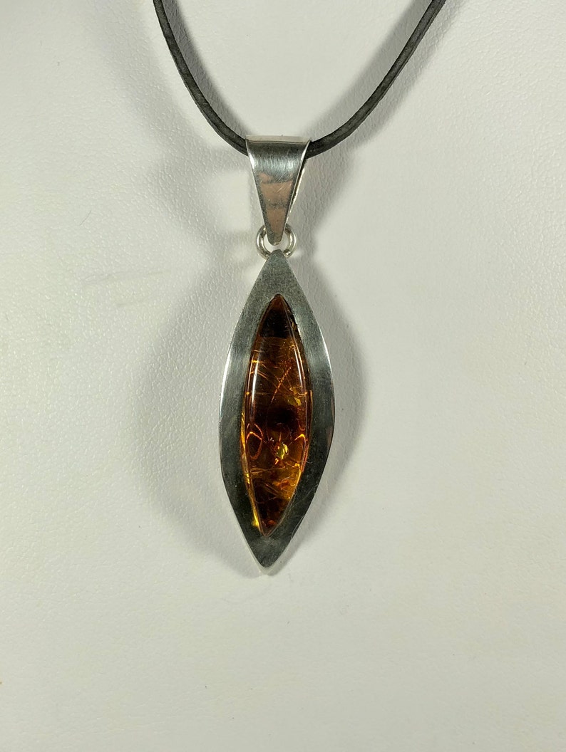 May include: A silver pendant necklace with a teardrop-shaped amber stone set in a silver frame. The necklace is on a black cord.