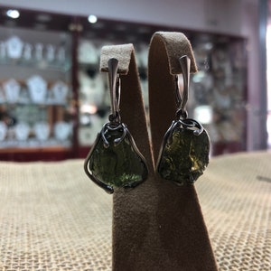 May include: A pair of silver earrings with green gemstone drops. The gemstones are irregularly shaped and have a rough, natural look.