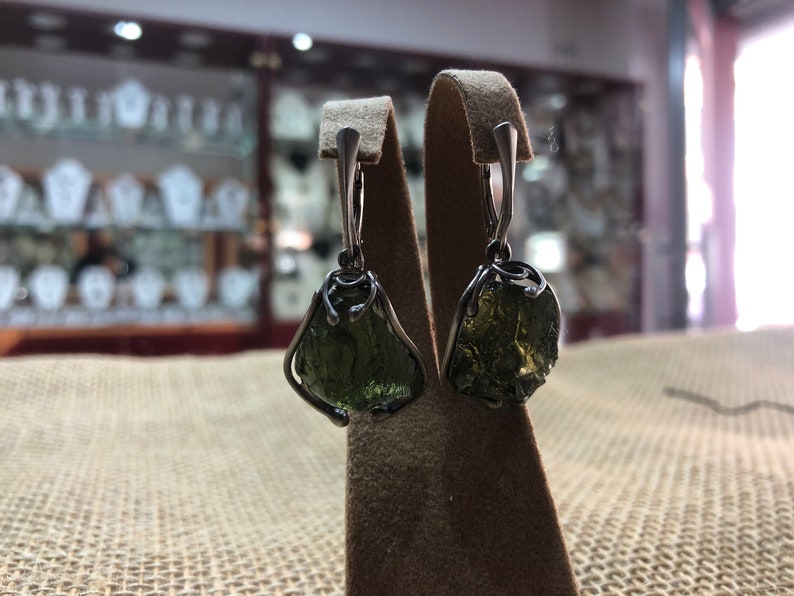 May include: A pair of silver earrings with green gemstone drops. The gemstones are irregularly shaped and have a rough, natural look.