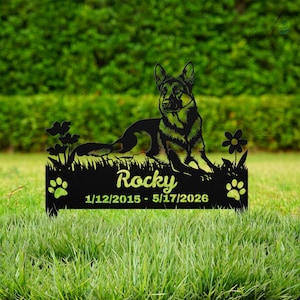 May include: A black metal memorial garden stake featuring a German Shepherd silhouette lying down, surrounded by flowers and paw prints. The text reads Rocky, 1/12/2015 - 5/17/2026, engraved on the base of this commemorative outdoor pet marker.