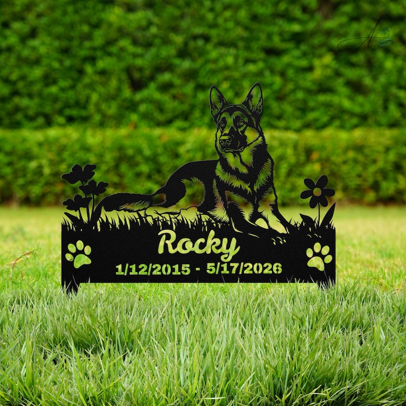 May include: A black metal memorial garden stake featuring a German Shepherd silhouette lying down, surrounded by flowers and paw prints. The text reads Rocky, 1/12/2015 - 5/17/2026, engraved on the base of this commemorative outdoor pet marker.