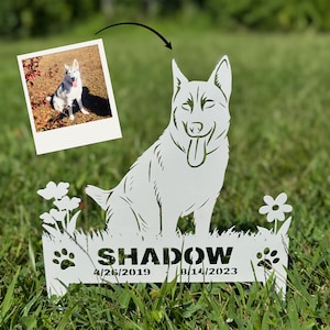May include: A white metal garden stake featuring a cutout silhouette of a dog with its tongue out, surrounded by flowers and paw prints. The text SHADOW is centered above the dates 4/26/2019 - 8/14/2023, with a small photo of the dog above.
