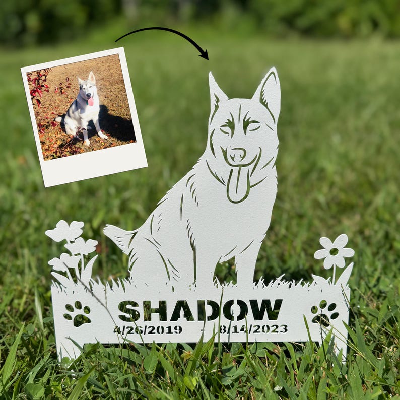 May include: A white metal garden stake featuring a cutout silhouette of a dog with its tongue out, surrounded by flowers and paw prints. The text SHADOW is centered above the dates 4/26/2019 - 8/14/2023, with a small photo of the dog above.