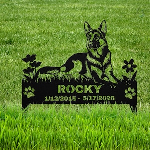 May include: A black metal garden stake featuring a silhouette of a German Shepherd dog lying down, flanked by flowers. The base includes the name ROCKY and the dates 1/12/2015 - 5/17/2026, with a paw print icon on each side of the text.