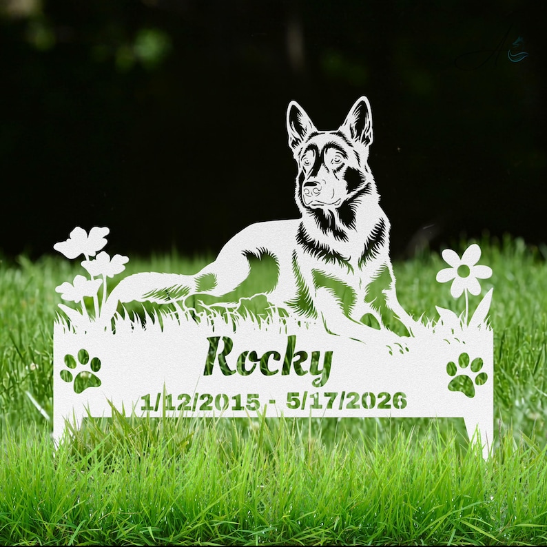 May include: A white metal garden stake featuring a cutout silhouette of a German Shepherd dog lying in grass with flowers. The base includes the name Rocky and the dates 1/12/2015 - 5/17/2026, flanked by two paw print cutouts on the left and right sides.