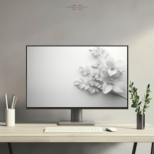 Op de afbeelding: Een witte computermonitor met een wit bloemenontwerp op het scherm. De monitor staat op een licht houten bureau met een wit toetsenbord en een witte muis. Er staat een kleine plant in een pot op het bureau.