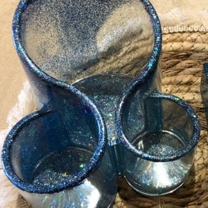 Könnte beinhalten: Ein blauer Glitzer-Make-up-Organizer mit drei Fächern. Der Organizer ist aus klarem Kunststoff und hat eine glitzernde Oberfläche.