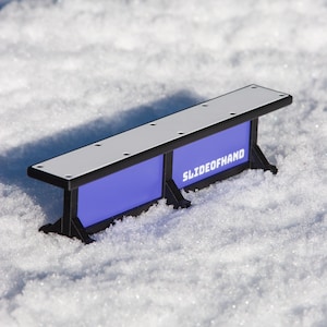 May include: A black and blue fingerboard ramp with a white top and the text "SLIDE OF HAND" printed on the side.