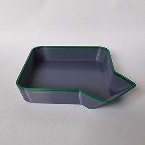 Puede incluir: Una bandeja de plástico gris con un borde verde. La bandeja tiene un pequeño pico en un lado.