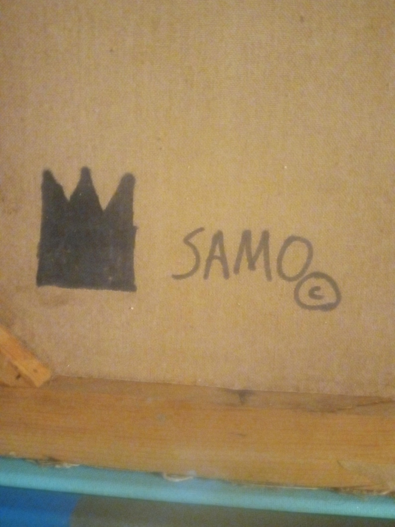 Puede incluir: Una corona negra y la palabra "SAMO" con un s&iacute;mbolo de copyright escrito en tinta negra sobre una superficie marr&oacute;n.