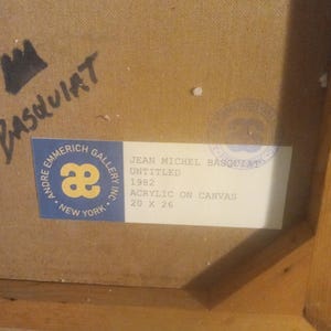 Puede incluir: Una etiqueta blanca con texto negro en un marco de madera. La etiqueta dice "Andre Emmerich Gallery Inc. New York" con un logotipo "ae" estilizado. La etiqueta tambi&eacute;n dice "Jean Michel Basquiat Untitled 1982 Acrylic on Canvas 20 x 26".