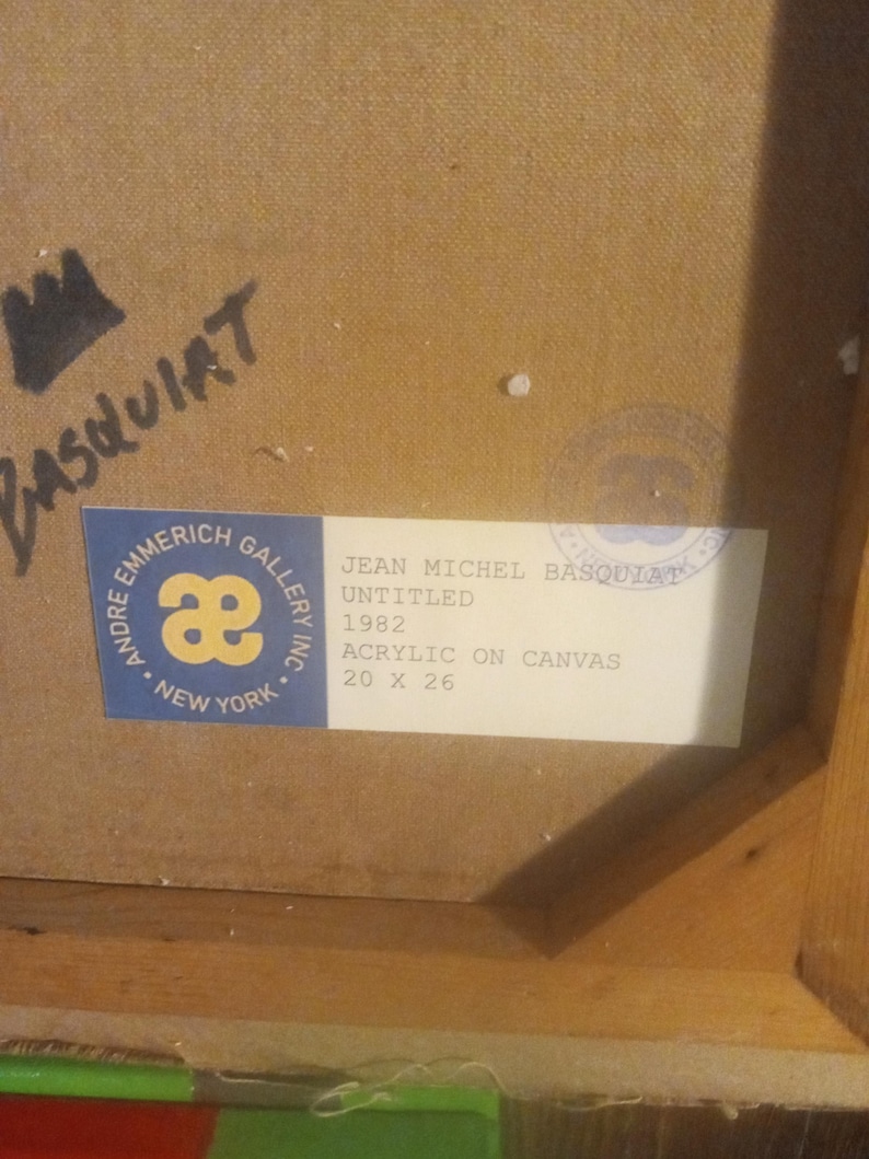 Puede incluir: Una etiqueta blanca con texto negro en un marco de madera. La etiqueta dice "Andre Emmerich Gallery Inc. New York" con un logotipo "ae" estilizado. La etiqueta tambi&eacute;n dice "Jean Michel Basquiat Untitled 1982 Acrylic on Canvas 20 x 26".