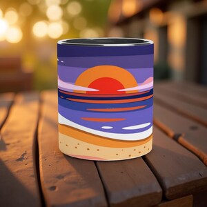 May include: Cylindrical tumbler with a sunset design. It depicts an orange sun, purple sky, and blue ocean, with a sandy beach at the bottom. The tumbler is placed on a wooden surface.