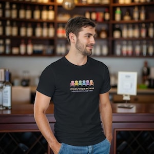 May include: Black t-shirt featuring a row of colorful Adirondack chairs above the text "PROVINCETOWN MASSACHUSETTS". The design is in pastel colors. The shirt is a crew neck style.