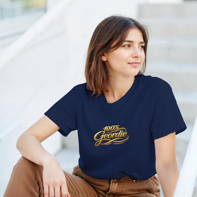 K&ouml;nnte beinhalten: Marineblaues T-Shirt mit dem Text "100% Geordie" in goldener Schrift. Das T-Shirt hat einen Rundhalsausschnitt und scheint aus einem weichen Material zu sein. Das Design ist mittig auf der Brust platziert.