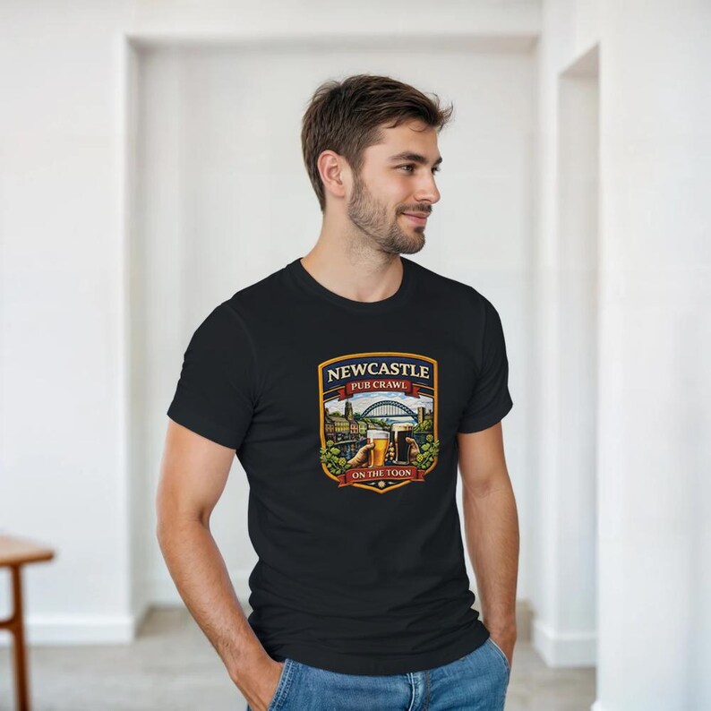 Pu&ograve; includere: T-shirt nero con una grafica colorata raffigurante una scena del Newcastle Pub Crawl. Il design include un ponte, edifici e bicchieri di birra, con il testo "Newcastle Pub Crawl" e "On the Toon". La maglietta &egrave; indossata da una persona.