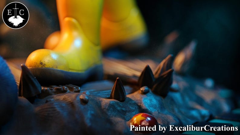 May include: A close-up of a figurine with yellow boots standing on a rocky surface with dark brown spikes. The base is painted in shades of gray and blue. The text "Painted by ExcaliburCreations" is visible at the bottom.